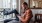 a man sits on a chair and rests his foot on a balcony railing as he looks at his phone in his room